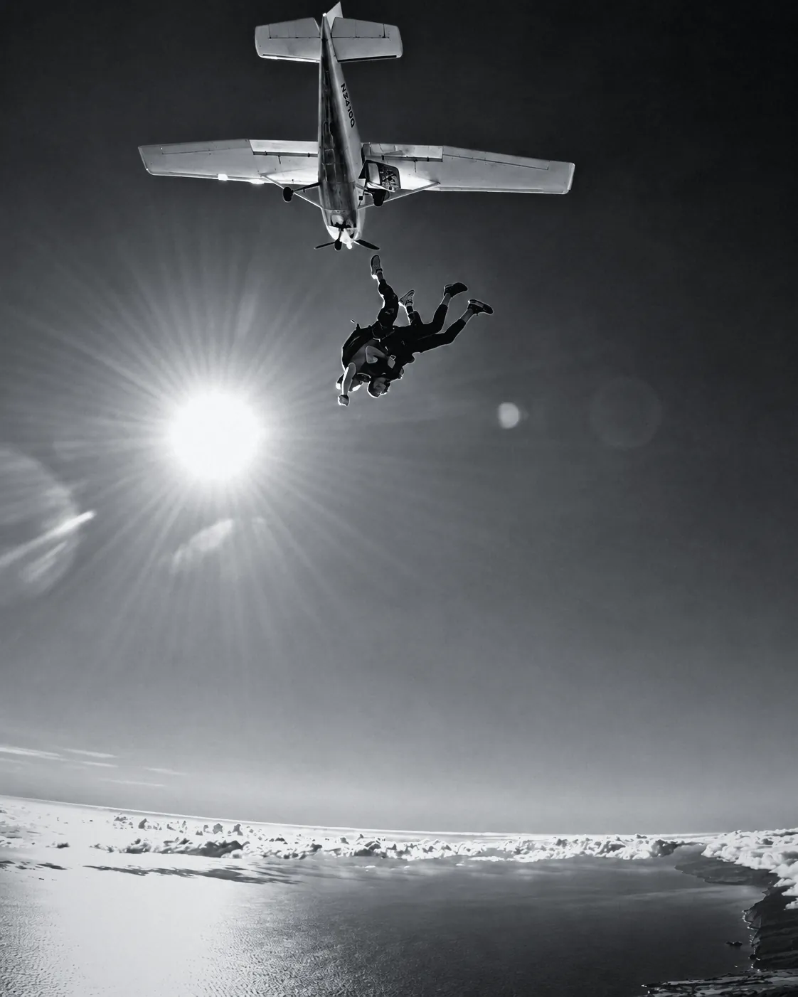 Houman Farzian leaving the plane on a tandem skydive, the sun behind him, black and white