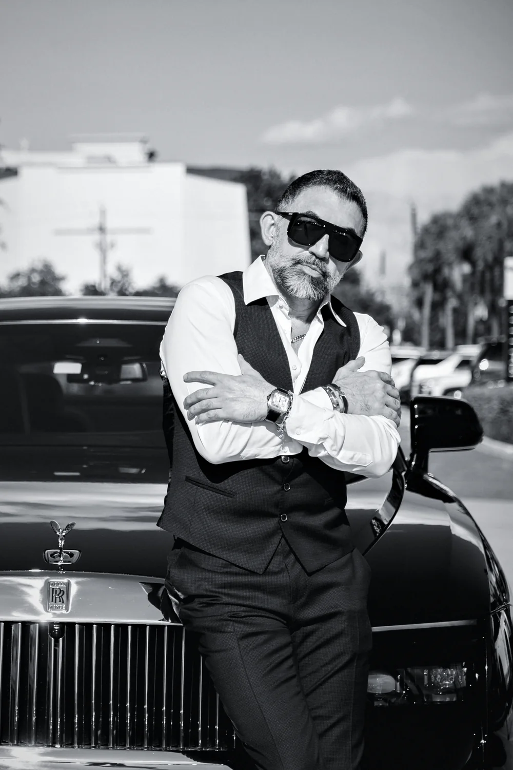Houman Farzian in sunglasses, arms crossed, leaning on the hood of his car, black and white